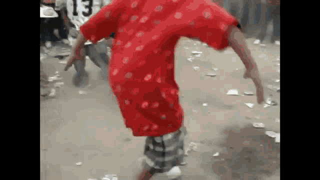 a man in a red shirt and plaid shorts is dancing on the street