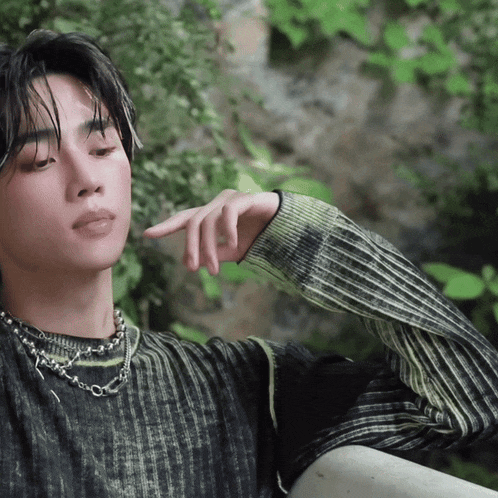 a close up of a person wearing a sweater and a necklace with their hand on their chin