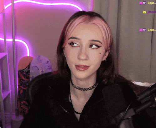 a girl with pink hair is sitting in front of a microphone with purple lights behind her