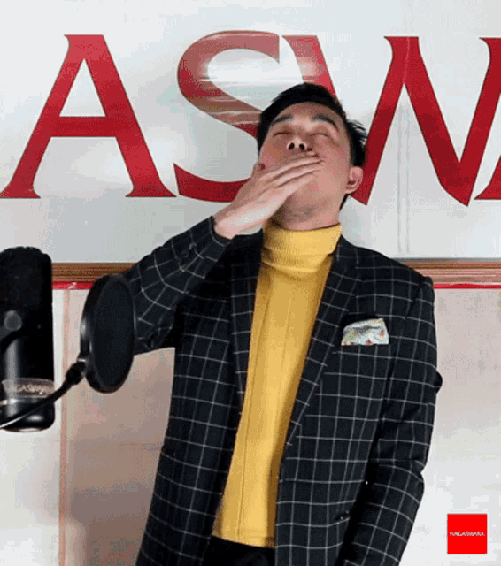 a man covering his mouth with his hand in front of a sign that says " asn "