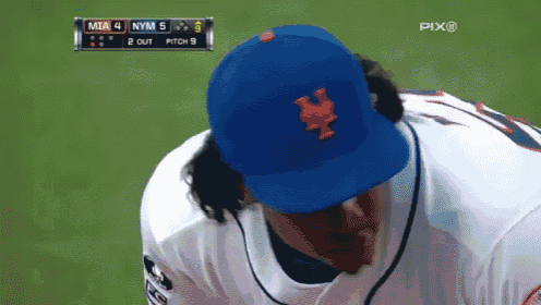 a baseball player wearing a blue ny mets hat looks down at something