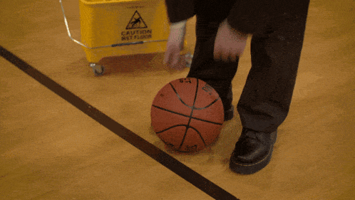 a man in a suit holds a basketball in front of a yellow mop bucket
