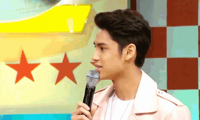 a young man is holding a microphone in front of a wall with stars