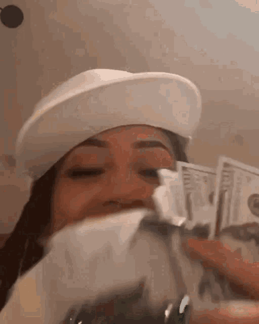 a woman wearing a hat is holding a bunch of money in her hand .