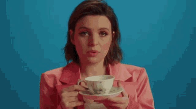 the woman is wearing a pink jacket and holding a cup of tea .