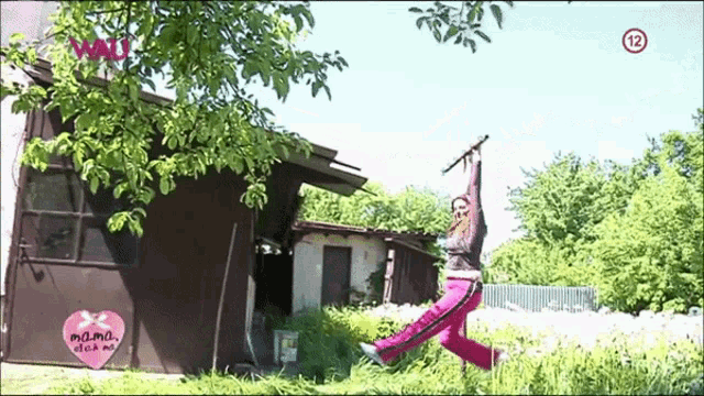 a woman is jumping in the air in front of a building with the number 12 on the bottom right