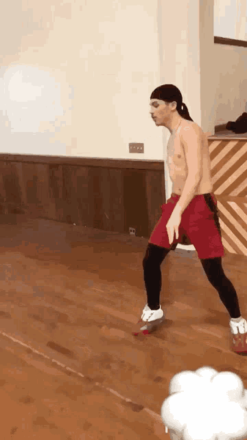a shirtless man in red shorts and white shoes is standing on a wooden floor