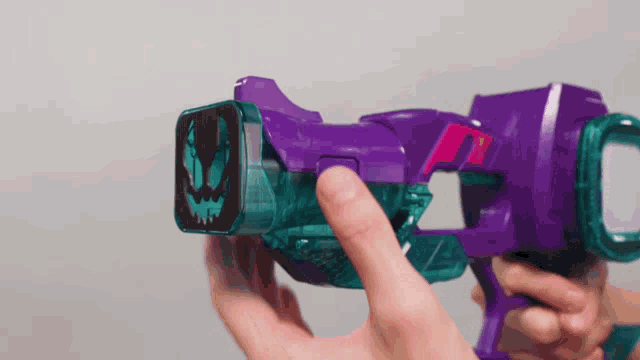 a person is holding a purple and blue toy gun with their finger .