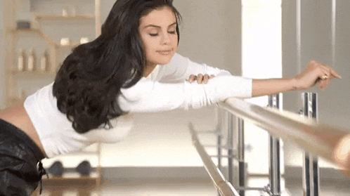 a woman is leaning on a bar in a gym while stretching her arms .