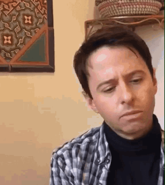 a man in a plaid shirt is making a funny face in front of a wall with a picture on it .