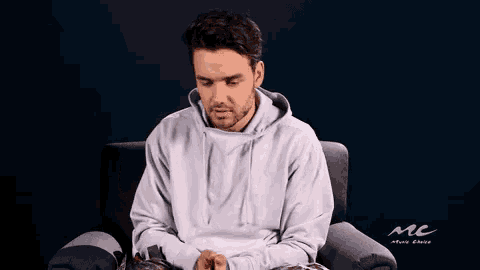 a man in a white hoodie is sitting in a chair holding something in his hands .