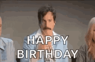 a man with a mustache is standing in front of a group of people and saying happy birthday .