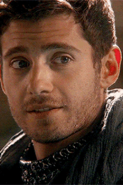 a close up of a man 's face with a beard wearing a scarf around his neck .