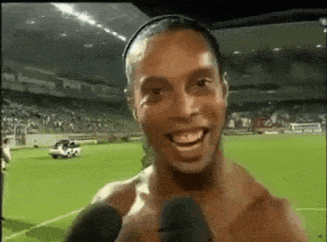 a shirtless soccer player is smiling and talking into a microphone on a soccer field .