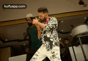 a man with a beard and glasses is dancing in a room with other men .