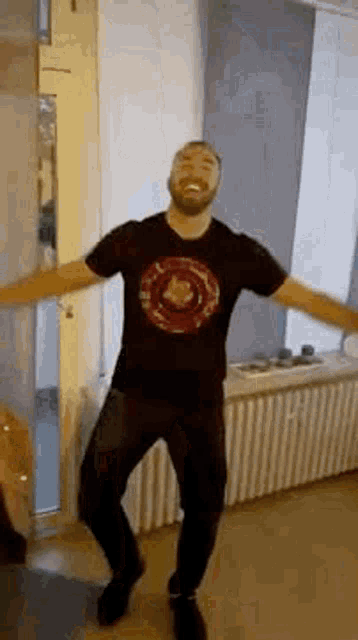 a man in a black t-shirt is dancing in a room with his arms outstretched .