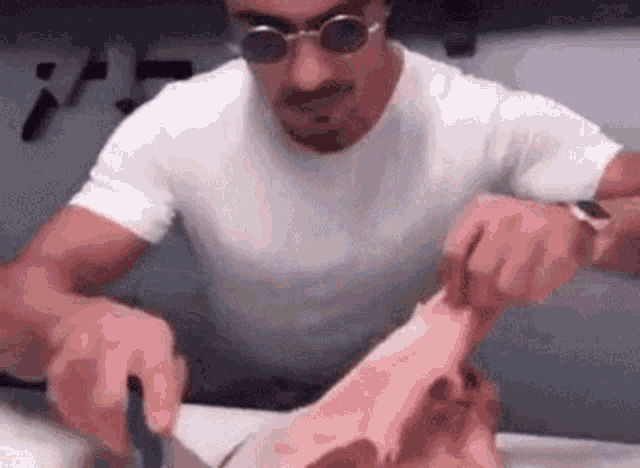 a man wearing sunglasses is cutting a large piece of meat on a cutting board .