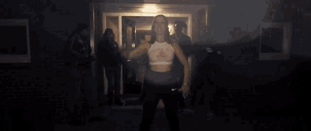 a woman in a crop top and black pants is standing in front of a group of people
