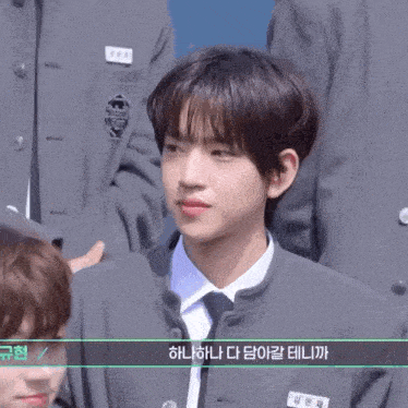 a young man in a suit and tie stands in front of a group of people with korean writing on them