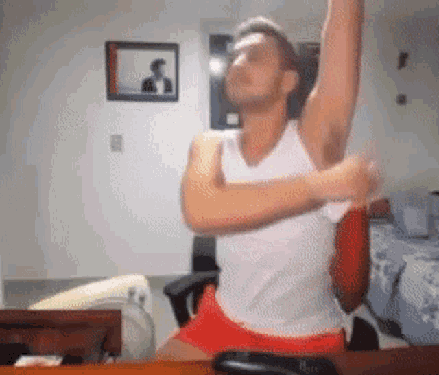 a man in a white tank top and red shorts is sitting in a chair with his arms outstretched