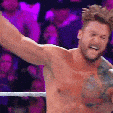 a shirtless wrestler is standing in a wrestling ring with his arms outstretched .
