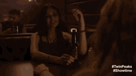a woman sitting at a table with a bottle of beer and a #twinpeaks #showtime hashtag