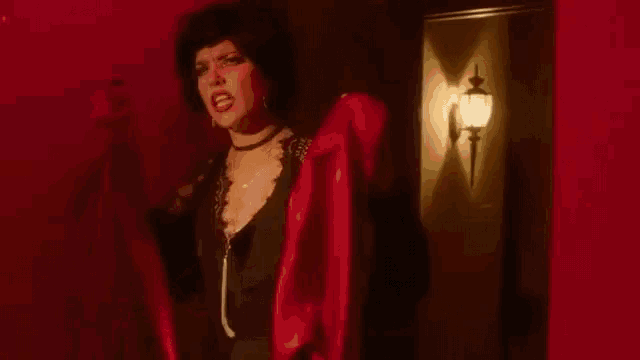a woman in a black dress is standing in a room with her mouth open and a light on the wall .