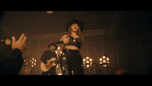 a woman in a cowboy hat sings into a microphone while a man plays a guitar
