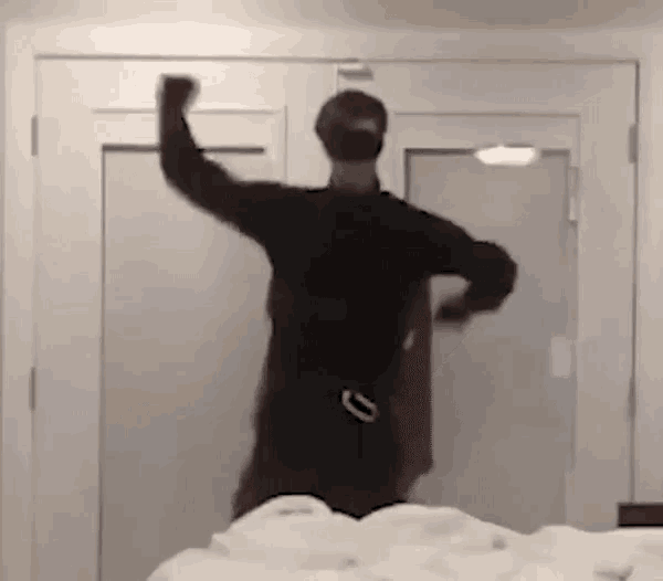 a man in a black shirt is dancing in front of a door in a bedroom .
