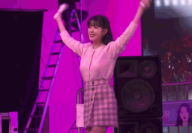 a woman in a pink plaid skirt is standing on a stage with her hands in the air .