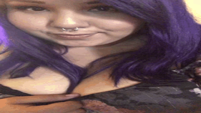 a woman with purple hair and a nose ring looks at the camera