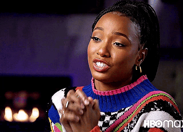 a woman wearing a colorful sweater and hoop earrings is clapping her hands .