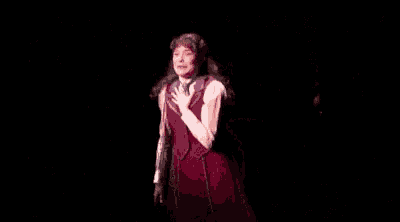 a woman is standing on a stage with her arms outstretched in a dark room .