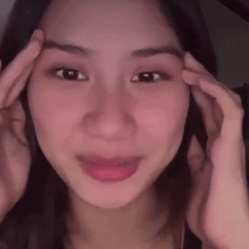 a close up of a woman touching her forehead with her hands .