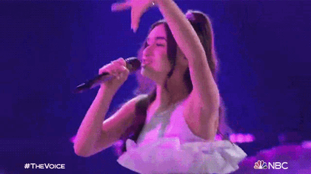 a woman in a white dress singing into a microphone