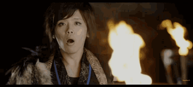a woman with a blue lanyard around her neck stands in front of a burning fire
