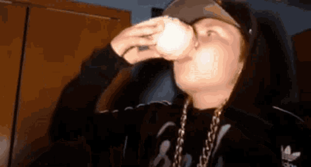 a person wearing a black adidas jacket is drinking from a glass