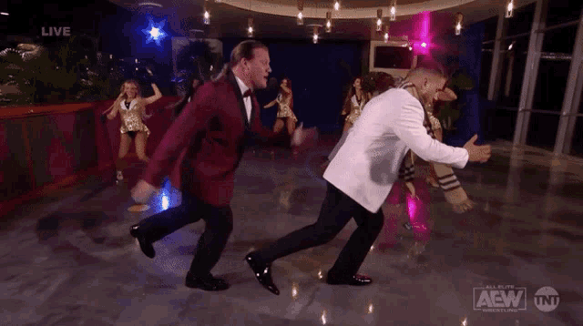 two men in tuxedos are dancing in a room with a live aew logo