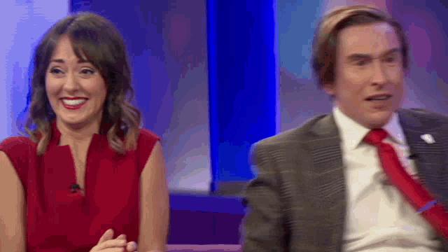 a man in a suit and tie sits next to a woman in a red shirt