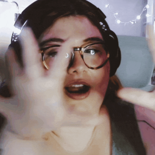 a woman wearing glasses and headphones making a stop sign