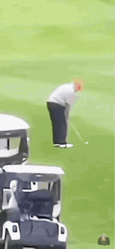 a man is playing golf on a golf course with a golf cart behind him .
