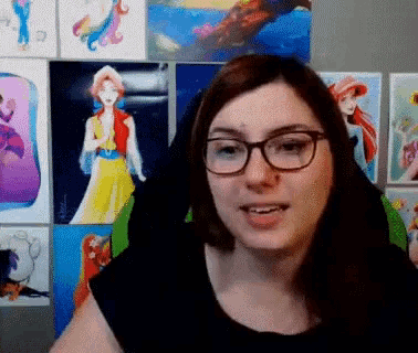 a woman wearing glasses and a black shirt stands in front of a wall of paintings