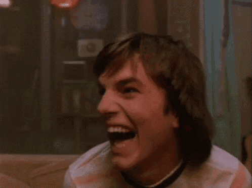 a young man is laughing while sitting on a couch in a dark room .