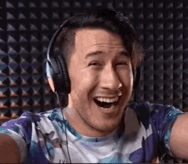 a man wearing headphones and a tie dye shirt is smiling .