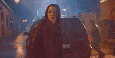 a woman is standing in front of a car with a gun in her hand .