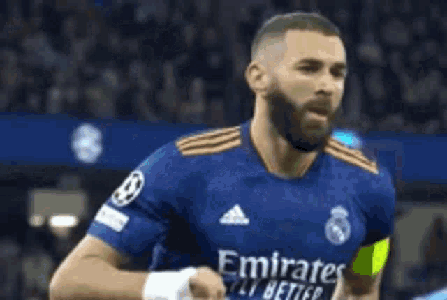 a man with a beard is wearing a blue emirates fly better soccer jersey .