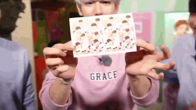 a man in a pink sweater is holding a card with a picture of a group of people on it .