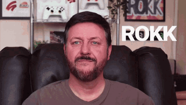 a man with a beard is sitting in a chair and the word rokk is on the wall behind him