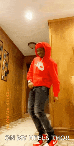 a man in a red hoodie is dancing in a hallway with the words `` on my heels tho '' .