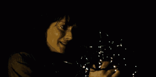 a woman is holding a string of christmas lights in her hands and smiling .